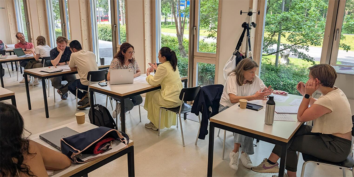 Doktorierende und Expertinnen sitzen sich jeweils Paarweise an einem Tisch gegenüber und diskutieren angeregt.