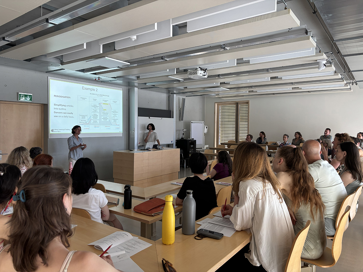 Personen in einem Seminarraum hören bei einer Präsentation zu.